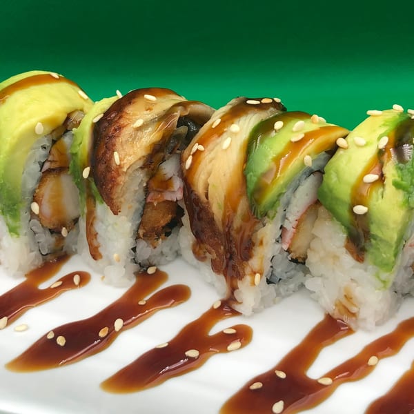 Sushi rolls with avocado, eel, shrimp tempura, and sesame seeds, drizzled with sauce.