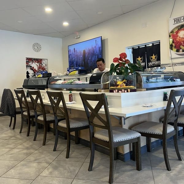Sushi chef behind a long counter with sushi display cases and bar stools at Kawaii Sushi.