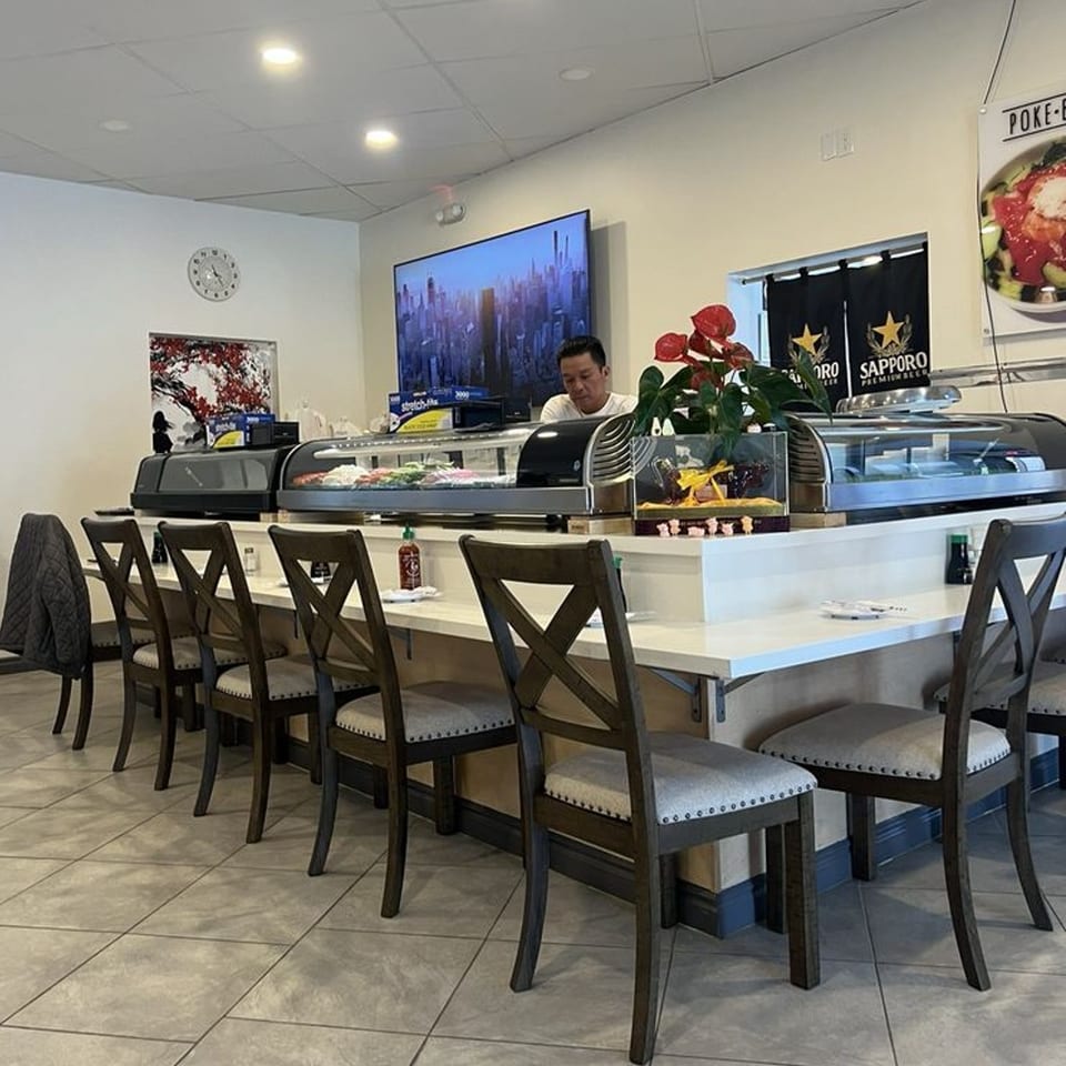 Sushi chef behind a long counter with sushi display cases and bar stools at Kawaii Sushi.