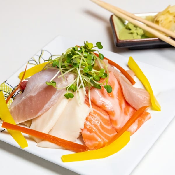Assorted sashimi with salmon, white fish, and tuna, garnished with sprouts and bell peppers.