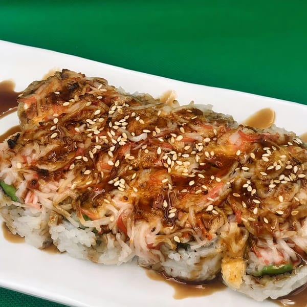 Kawaii Sushi's baked sushi roll, topped with crab, sauce, and sesame seeds, on a white plate.