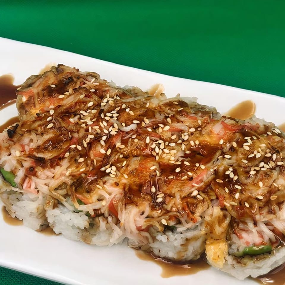 Kawaii Sushi's baked sushi roll, topped with crab, sauce, and sesame seeds, on a white plate.