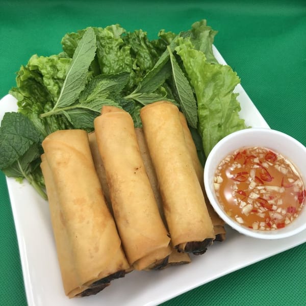 Crispy fried spring rolls with fresh lettuce, mint, and a side of chili dipping sauce.