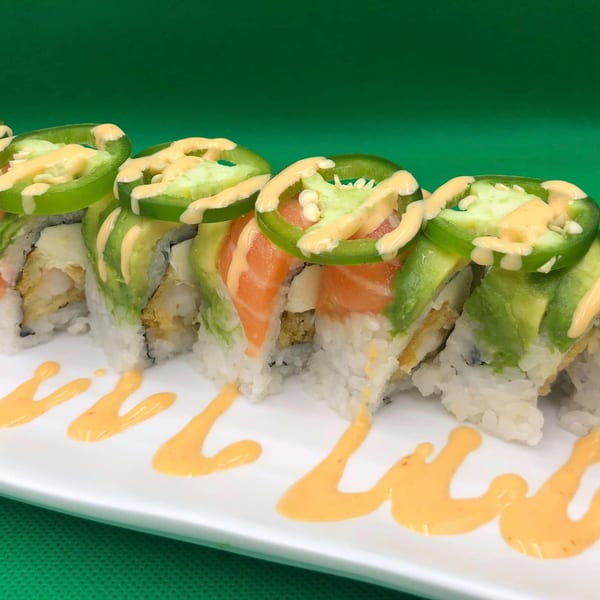 Sushi rolls with avocado, salmon, and jalapeño slices, drizzled with sauce on a white plate.