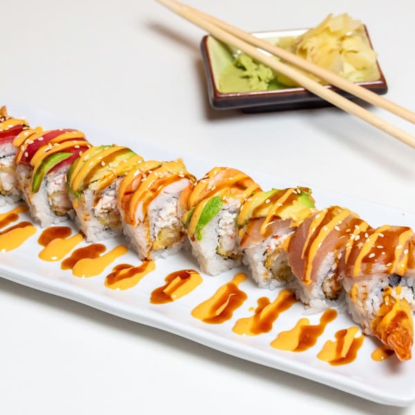 A long plate of Kawaii Sushi's colorful sushi rolls with sauces, chopsticks, wasabi, and ginger.
